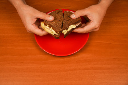 Food. Tasty sandwich. Hands holding sandwich with ham, bacon, cheese, lettuce, tomatoes. Close-up of man eating sandwich. Close-up image of a male cooking and holding sandwich.の写真素材