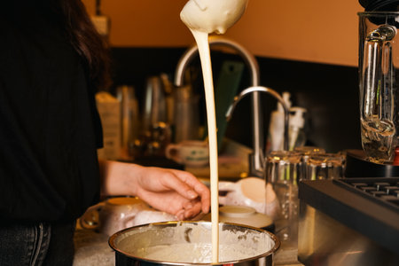 Liquid dough poured waffle iron machine to prepare Belgian waffle. Cooking process. Food preparation. Making Belgian waffles. Female hand pours dough into waffle maker in kitchen at home. Breakfast.の写真素材