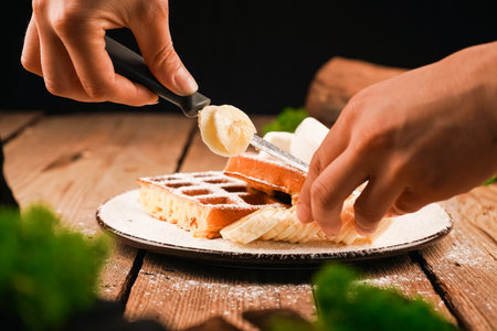 Adding banana on waffle. Topped powdered sugar. Homemade simple pastries. Belgian waffles on wooden table. Belgian waffles on a white plate. Waffles on plate. Ice-cream topping. Cooking process.の写真素材