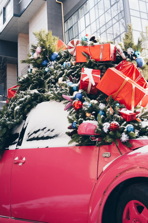 New Year and magic Christmas decorated exterior with retro red car with many gifts and festive lights and garlands outside with skyscraper on the background.の写真素材