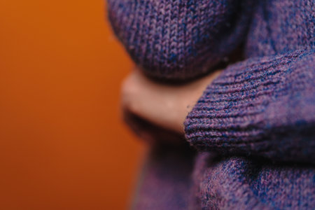 A woman in purple knitted sweater put her hand under elbow, without her face seen, closeup shot. Sign of closeness and uncertainty. Non-verbal sign language, horizontal picture.の写真素材