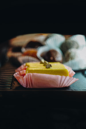 A view of a display of assorted pastries, inside a bakery shop. Yellow beautiful cheese pastry in pink covering laying down on a black plate, side view.の写真素材