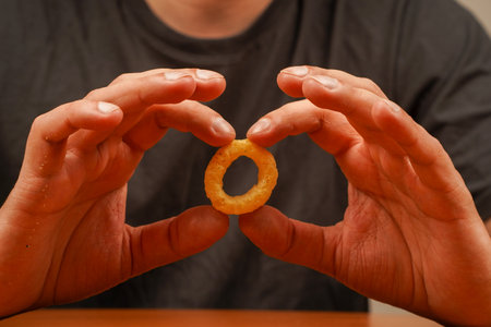 Cooked tasty appetizer meal. Fried rings. Corn onion rings. Unhealthy food. Man holds onion ring. Eating onion rings. Onion ring. Deep fried onion rings. Snack for beer. Fast food. Junk food.の写真素材