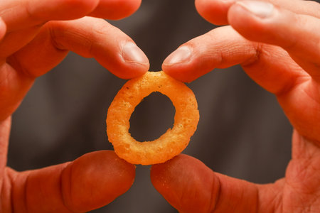 Man holds onion ring. Eating onion rings. Onion ring. Deep fried onion rings. Snack for beer. Fast food. Junk food. Cooked tasty appetizer meal. Fried rings. Corn onion rings. Unhealthy food.の写真素材