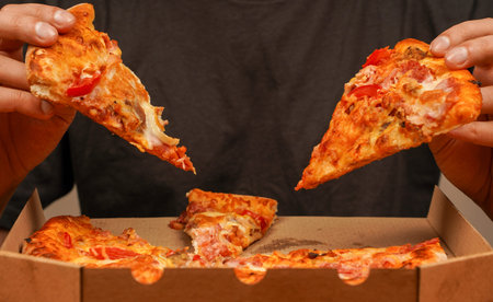 Concept of takeaway. Fast food order. Restaurant advertising. Delicious cheesy pizza. Pizza. Unhealthy food. Junk food. Fatty food. Tasty food at pizzeria. Hand taking pizza slice, close up view.の写真素材