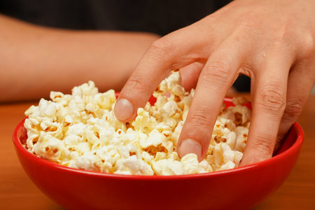 Flavored spicy popcorn scattered on table surface. Bowl of tasty popcorn on wooden table. Delicious snack to eat in the cinema. Salted popcorn. Popcorn. Fast food. Junk food. Snack for cinema.の写真素材