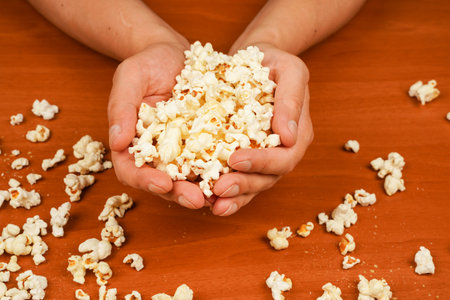 Salted popcorn. Popcorn. Fast food. Junk food. Snack for cinema. Popcorn scattered on table surface. Delicious snack to eat in the cinema. Flavored spicy popcorn in mans hands.の写真素材