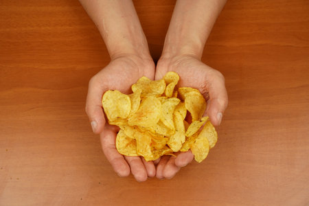 Calories. Obesity. American food. Fast food. Junk food. Unhealthy lifestyle. Man eating potato chips. Hand holds potato chips. A view of a hand holding a stack of ridged potato chips.の写真素材