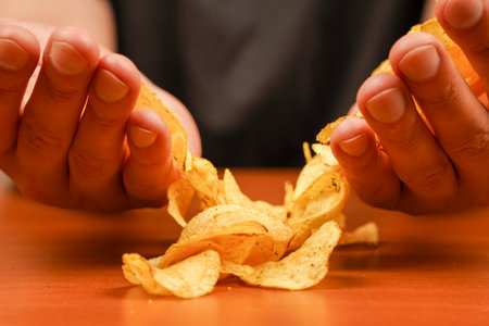 Fast food. Junk food. Unhealthy lifestyle. Man eating potato chips. Hand holds potato chips. A view of a hand holding a stack of ridged potato chips. Calories. Obesity. American food.の写真素材