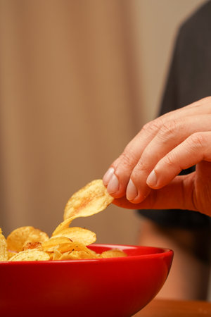 Fast food. Junk food. Unhealthy lifestyle. Calories. Obesity. American food. A view of a hand taking potato chips out of bowl. Hands holds potato chips. Man eating potato chips.の写真素材