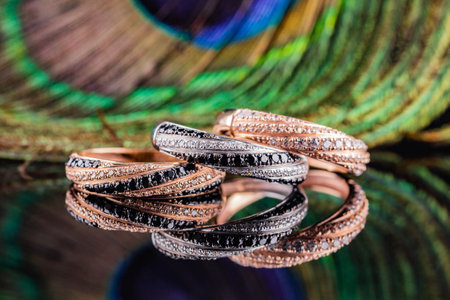 Wedding rings are reflected in the mirror. A set of three rings on a background of peacock feathers. Gold and silver rings with black and white stones.の写真素材