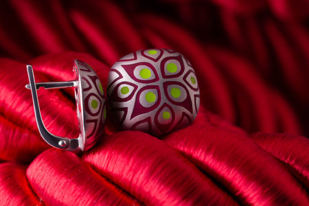 Two earrings with patterns. Jewelry on a background of red twisted rope. Round earrings close-up on a red background. Ethnic earrings with carving.の写真素材