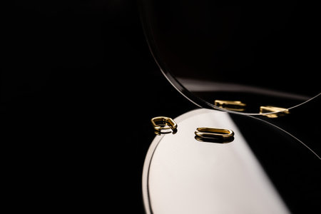 A metal jewelry in a mirror close-up. Beautiful stylish jewellery. Gold earrings on a black background.の写真素材