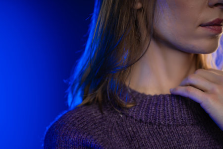 Female with red hair in purple knitted sweater touching her sweaters collar with some blue light and blue background.の写真素材