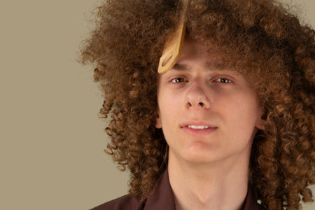 Closeup photo of curly young guy. Smiling curly haired young man with brush in his hair, studio shot.の写真素材