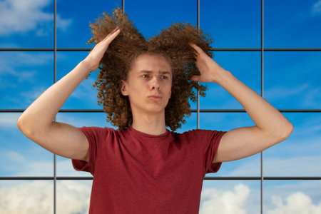Caring and styling his waving hair. Standing over nice studio background. Man holding pieces of his...