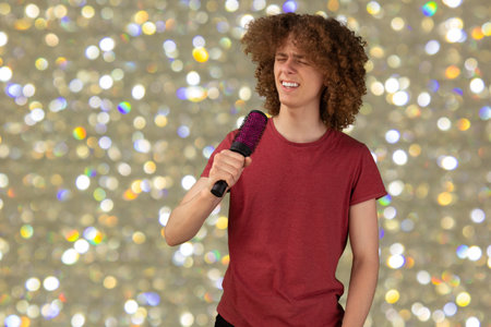 Growing long healthy hair. Male hair care problems. Fully standing and singing in brush like in microphone young man with curly hair on glittery background.の写真素材