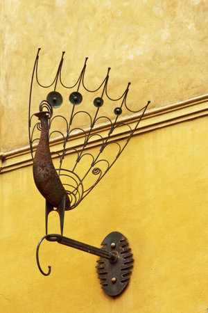 Prague, Czech Republic - May 11, 2019: Iron peacock figure on stick as a building decoration with the background of yellow wall. Decoration of old European architecture. Old buildings of Prague.の写真素材