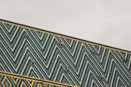 Vienna, Austria - May 12, 2019 Intricate zigzag pattern adorns sloped roof of historical building, featuring mix of green, white, blue, tiles. Small dormer windows peek out from patterned surface.の写真素材
