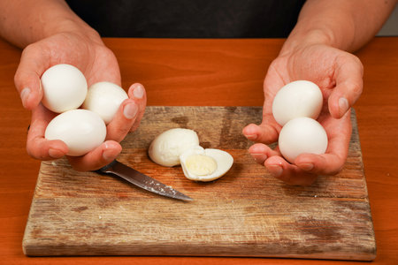 Preparing food. Horizontal photo. Vegetarian. Protein. Healthy food. Board with boiled eggs on table, closeup. . Man holding boiled eggs over wooden board. Boiled eggs.の写真素材