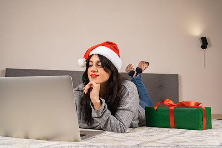 A young woman in a red Santa Claus hat is sitting in front of a laptop. Online shopping concept....