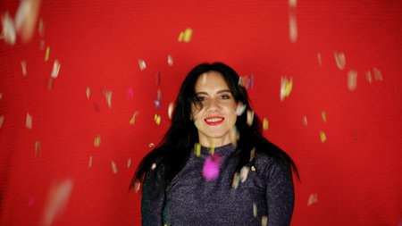 Cheerful beautiful brunette girl blowing confetti from her hands. Celebration of the holiday. Festive New Years atmosphere. Fun event. Christmas concept.の写真素材