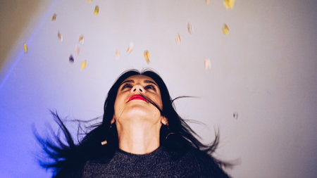 Cheerful beautiful brunette girl blowing confetti from her hands. Celebration of the holiday. Festive New Years atmosphere. Fun event. Christmas concept.の写真素材