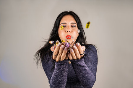 Cheerful beautiful brunette girl blowing confetti from her hands. Celebration of the holiday. Festive New Years atmosphere. Fun event.の写真素材
