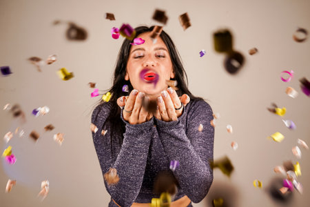Cheerful beautiful brunette girl blowing confetti from her hands. Celebration of the holiday. Festive New Years atmosphere. Fun event. Christmas concept.の写真素材