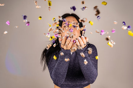 Cheerful beautiful brunette girl blowing confetti from her hands. Celebration of the holiday. Festive New Years atmosphere. Fun event. Christmas concept.の写真素材