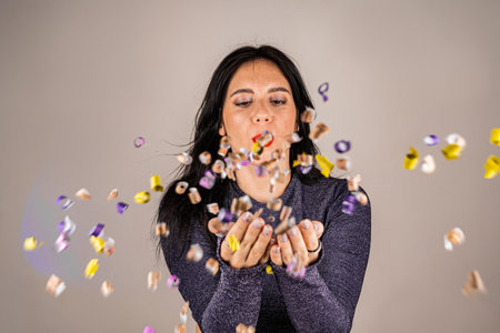 Cheerful beautiful brunette girl blowing confetti from her hands. Celebration of the holiday. Festive New Years atmosphere. Fun event. Christmas concept.の写真素材