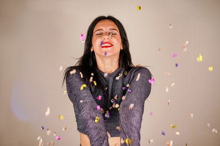 Cheerful beautiful brunette girl blowing confetti from her hands. Celebration of the holiday. Festive New Years atmosphere. Fun event. Christmas concept.の写真素材