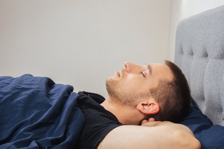 Top view of a handsome young man sleeping comfortably on the bed at night in his bedroom. Sleep in different positions. Bachelor bedroom. Deep sleep.の写真素材
