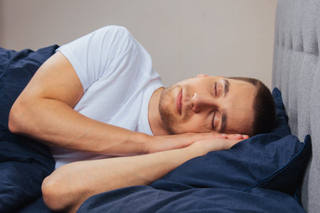 Top view of a handsome young man sleeping comfortably on the bed at night in his bedroom. Sleep in different positions. Bachelor bedroom. Deep sleep.の写真素材
