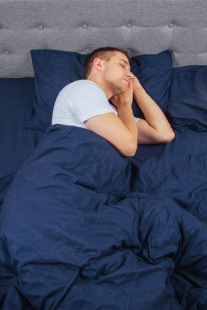 Top view of a handsome young man sleeping comfortably on the bed at night in his bedroom. Sleep in...