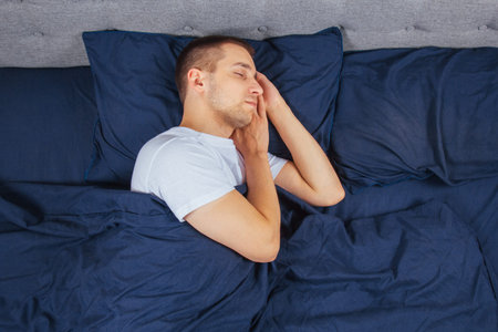 Top view of a handsome young man sleeping comfortably on the bed at night in his bedroom. Sleep in...