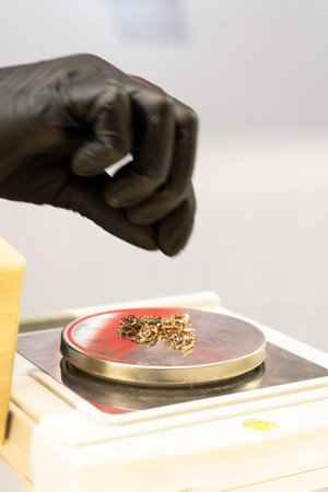 Hand take jewelry on the digital scale, close up. Hand in black glove puts gold on scales. Selective...