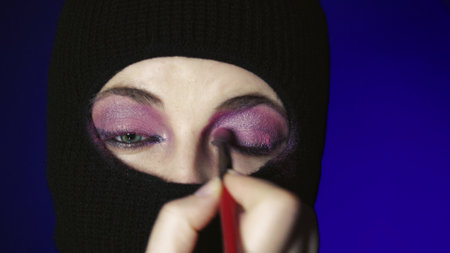 Fashionable beautiful girl in a balaclava. Fashion mask on beautiful female models. Girl in a black balaclava. Fashionable mask on a beautiful woman with colored make-up.の写真素材