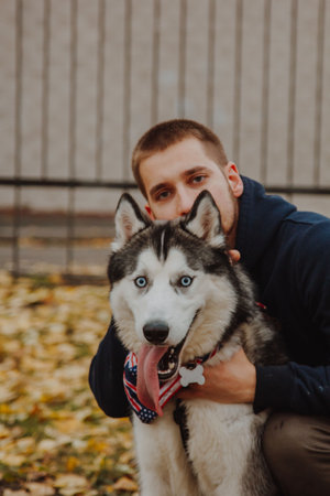 A man hugs a husky by the neck. A guy and a dog pose close-up on an autumn background.の写真素材