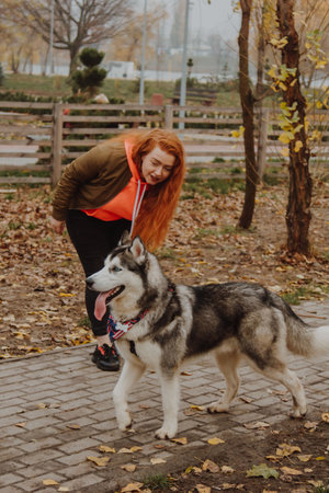 A young girl with long red hair plays with a husky dog. The process of integration of the individual into the social system. A woman walks her dog in the park.の写真素材