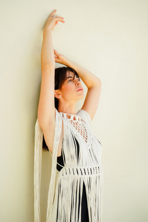 A brunette in a white boho cape poses near a white wall.の写真素材