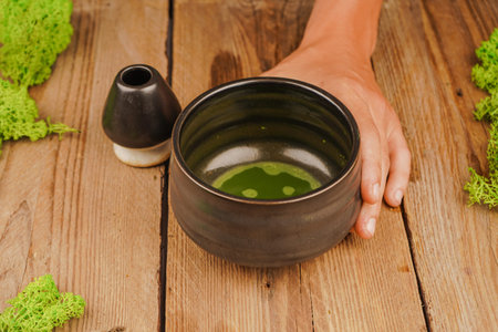 Traditional bamboo matcha whisk held in hand. Matcha utensils on wooden table. Perfect for tea culture, relaxation and natural life.の写真素材