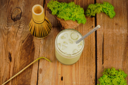 A close-up shot of a bamboo matcha whisk resting on a matcha table, symbolizing mindfulness and tradition. A full glass of iced matcha latte.の写真素材