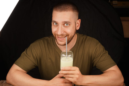 A man in an upbeat mood holds a glass of matcha latte with a straw. Perfect for a tea-related...