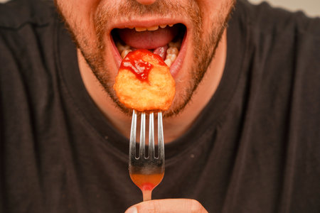 A close-up of a hand holding a crispy nuggets on a fork, perfect for depicting the enjoyment of food. The nuggets are dipped in red sauce, ketchup.の写真素材