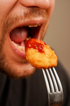 A close-up of a hand holding a crispy nuggets on a fork, perfect for depicting the enjoyment of food. The nuggets are dipped in red sauce, ketchup.の写真素材