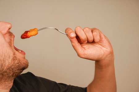 Freshly prepared nuggets held in hand, skewered on a fork, ready to be enjoyed, symbolizing the pleasure of fast food. Nuggets are slathered with ketchup.の写真素材