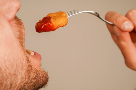 Freshly prepared nuggets held in hand, skewered on a fork, ready to be enjoyed, symbolizing the pleasure of fast food. Nuggets are slathered with ketchup.の写真素材
