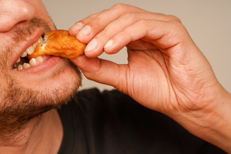A crunchy fried nugget held close to a mans mouth, emphasizing its appetizing appeal. A close-up shot of a man savoring a golden, crispy bite of comfort food.の写真素材