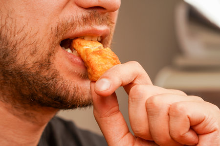 A crunchy fried nugget held close to a mans mouth, emphasizing its appetizing appeal. A close-up shot of a man savoring a golden, crispy bite of comfort food.の写真素材